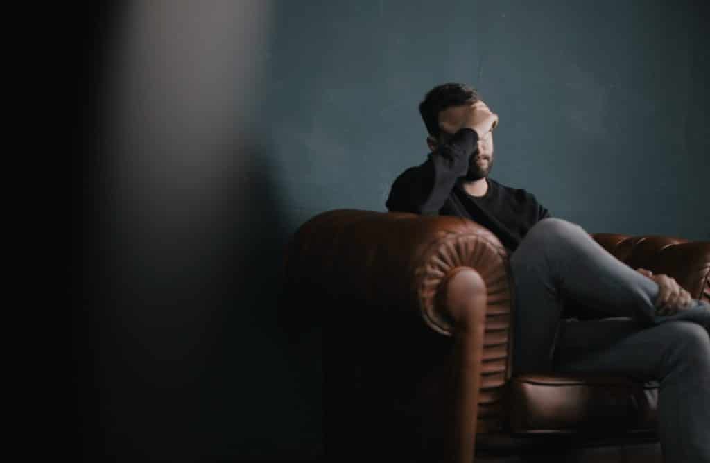 un homme se tient la tête assis sur un canapé